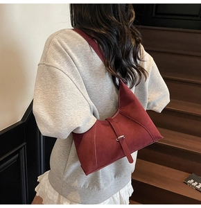 Close-up of a burgundy suede crescent hobo bag worn on the shoulder in a lifestyle setting
