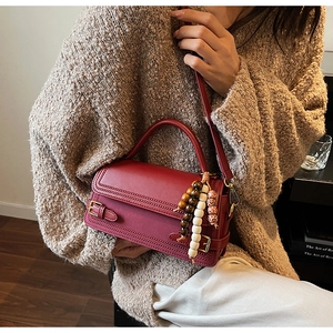 Detail of red leather square handbag with wooden bead charm and crossbody strap