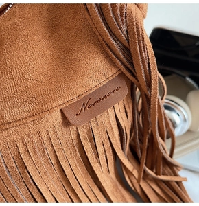 Dettaglio della borsa in pelle scamosciata caramello con frange boho e logo del marchio