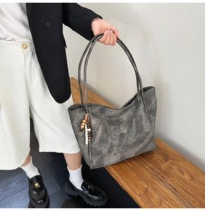 Detail view of large charcoal tote bag with vintage texture and wooden bead charm on handle