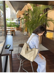 Detail of light khaki tote bag with beaded pendant and metal ring in outdoor cafe setting