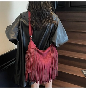 Dettaglio macro della pelle scamosciata bordeaux e frange fitte sulla borsa hobo
