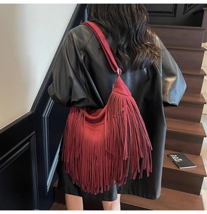 Detail of burgundy suede shoulder bag featuring long fringe tassels on a female model