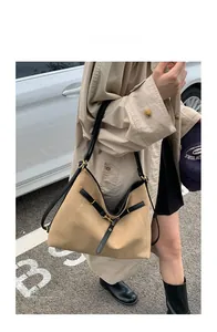 Detail of a large beige suede tote bag with black leather straps on a model outdoors