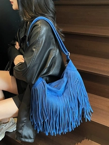 Borsa a spalla blu in camoscio con frange boho indossata da una modella su scale