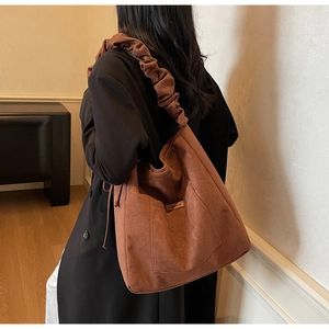 Detail of soft brown suede bucket bag featuring a unique pleated wide shoulder strap design
