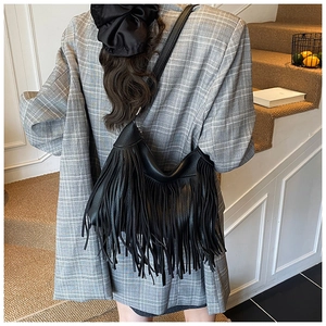 Détail du sac seau noir en cuir à longues franges sur une veste à carreaux