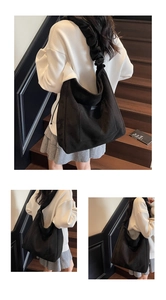 Close-up of a large black corduroy tote bag with ruffled shoulder strap on wooden stairs