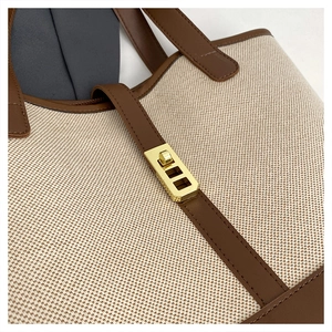 Macro shot of canvas tote bag featuring brown leather trim and golden metal turn-lock buckle
