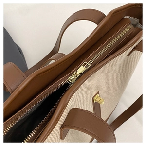 Close-up of golden zipper and leather trim detail on beige canvas tote bag