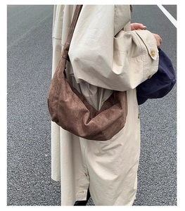 Sac croissant en daim marron porté en mode lifestyle avec un trench-coat chic