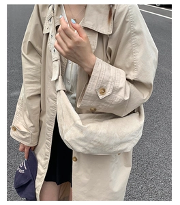 Détail d'un sac demi-lune en daim beige minimaliste porté avec un trench-coat élégant oversize