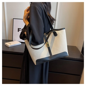 Detail of a large canvas tote bag with black leather trim and gold metal buckle closure