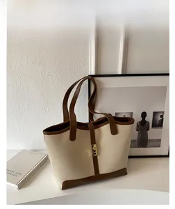 Detail of canvas tote bag with brown leather accents and gold metal lock on front