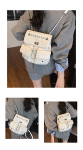 Detail of cream white backpack featuring metal chain straps and twist lock closure