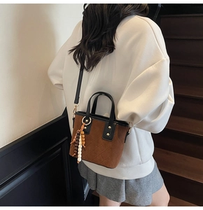 Borsa tote in camoscio marrone con trapuntatura e nappa mostrata su modella in interno moderno