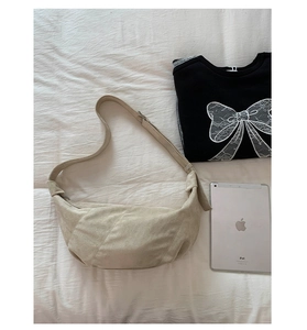 Détail du sac croissant en daim beige montrant la texture lisse à côté d'un iPad et pull