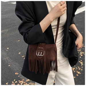 Close-up detail of brown suede fringe saddle bag worn as a crossbody by a model in black.