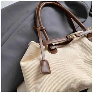 Close-up of off-white corduroy tote bag featuring brown leather straps and metal buckles