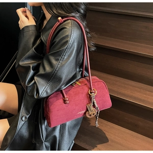Detail of dark red suede cylinder bag with gold abacus pendant on a leather shoulder strap