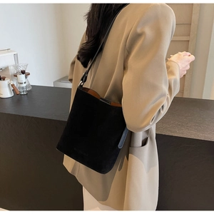 Detail of black suede tote bag with brown interior lining and buckle closure shown on model