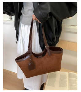Detail of brown suede tote bag with leather straps held by a model in a minimal setting