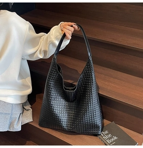 Close-up of black woven leather hobo shoulder bag on a wooden staircase background