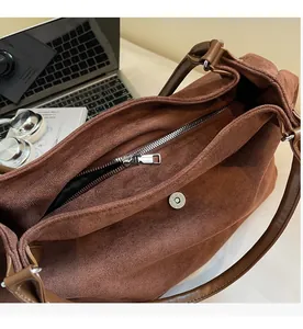 Detail view of smooth metal zipper and magnetic snap closure on brown suede tote bag