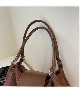 Detail of a brown suede tote bag featuring a wide leather handle and silver metal rings