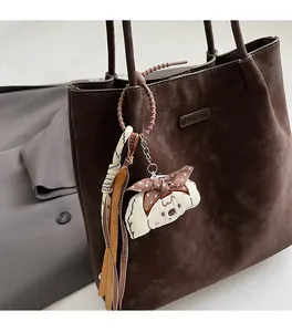 Detail of a plush dog charm with a brown polka dot bow on a large brown shoulder bag