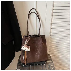 Detail of a brown suede tote bag featuring a leather logo patch and a cute puppy charm