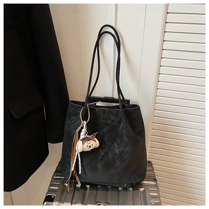 Detail of black leather tote bag featuring a textured finish and white puppy bag charm