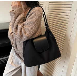 Detailed view of the black canvas and leather tote bag worn by a model in a minimal setting