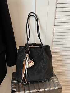 Black large capacity matte tote bag with plush charm on a silver metallic suitcase
