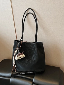 Minimalist black suede tote bag with cute puppy charm and ribbon on leather chair