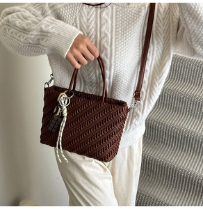 Dettaglio borsa a tracolla plissettata marrone scuro con charm cioccolato su maglione