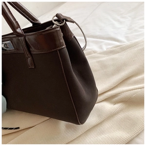 Detail of dark brown canvas tote bag featuring leather handles and silver metal clasp