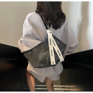 Detail of black pleated tote bag with branded cream shoulder strap shown on model