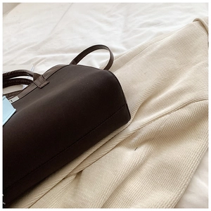 Detail of dark brown leather tote bag with blue trim accent on a soft white background