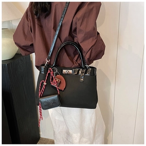 Detail of black tote bag with braided charm and leather trim shown on model