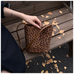 Gros plan du sac seau léopard avec bandoulière en cuir sur un banc avec feuilles d'automne
