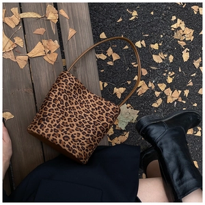 Gros plan du sac seau à motif léopard sur un banc en bois avec des feuilles de ginkgo