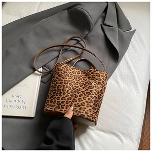 Détail d'un sac seau léopard posé sur un blazer gris avec un livre blanc déco