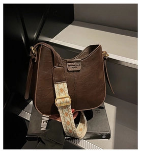 Detail view of brown vintage half-moon bag featuring a colorful wide jacquard strap