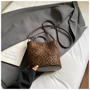 Détail du sac seau léopard avec poignées en cuir et bandoulière sur fond de tissu blanc