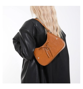 Detail of tan leather underarm bag featuring lace-up bow and silver metal rivets