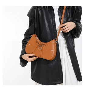 Close-up of brown PU leather shoulder bag with cross-lace design and metal rivets detail