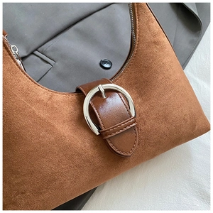 Détail d'un sac demi-lune en daim marron avec boucle argentée sur une veste grise