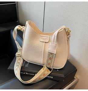 Close-up of a cream saddle bag with a wide ethnic jacquard strap on an art book