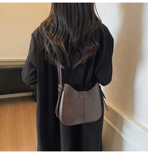Detail of dark brown leather hobo bag with vintage strap worn on a black coat